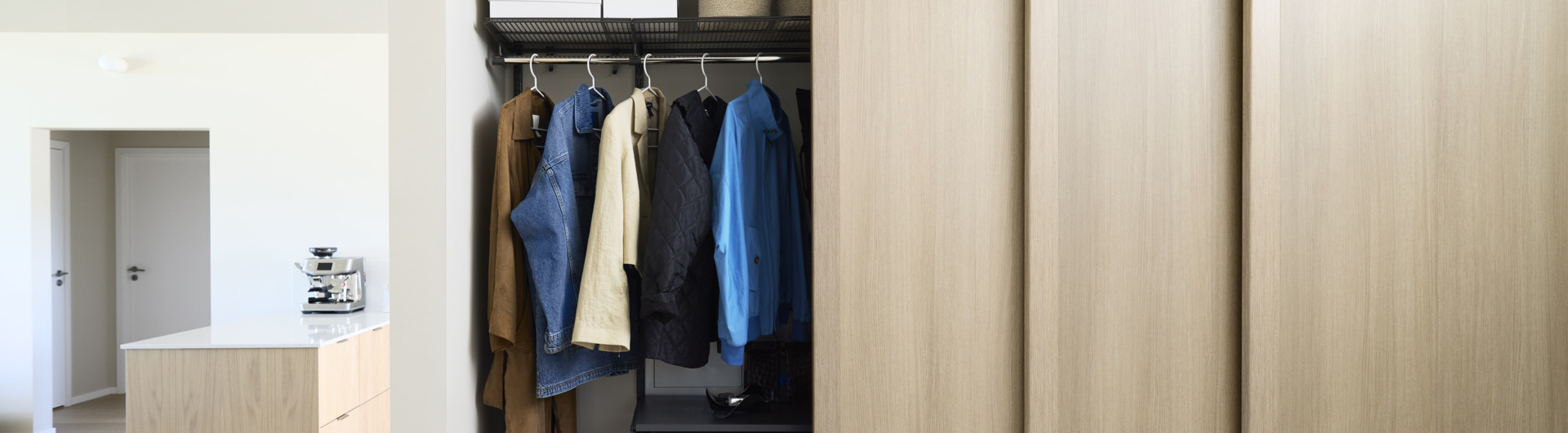 Eteinen, jossa on Elfa-vaatekaappi ja Grace-liukuovet, joiden täyte on vaaleaa tammea.